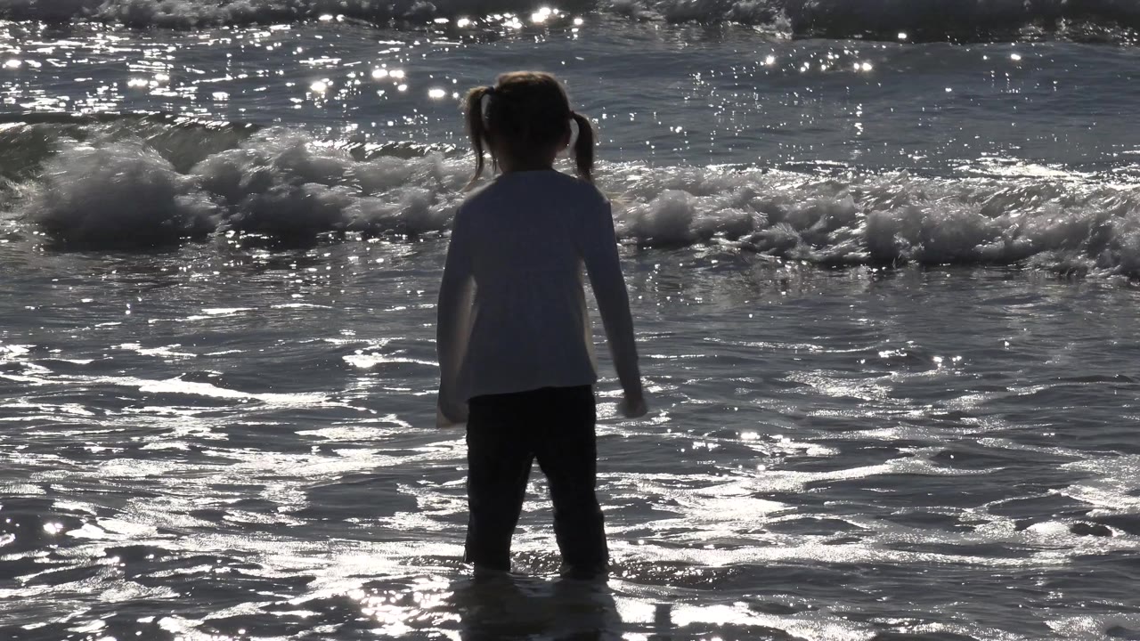 Child seen from behind near a breaking wave.