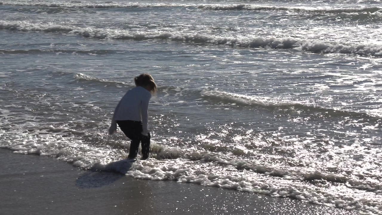 At Huntington Beach, California, the young girl stands partly turned toward the ocean as a thin foamy wave breaks around her lower legs.