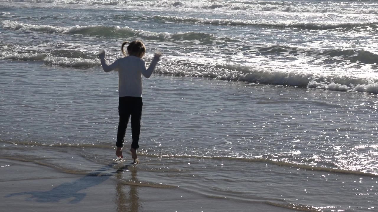 Girl jumping in shallow beach water.