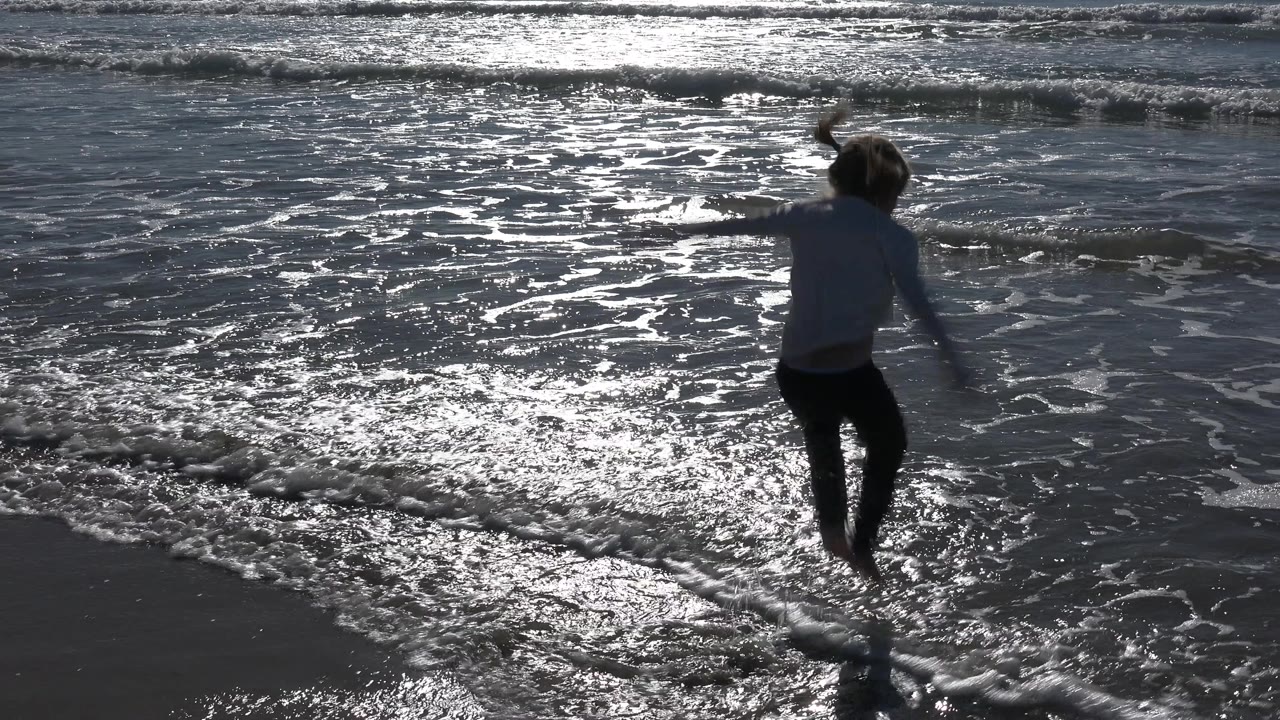 At Huntington Beach, California, the child lands near a narrow line of foam while the water surface glints strongly behind them.