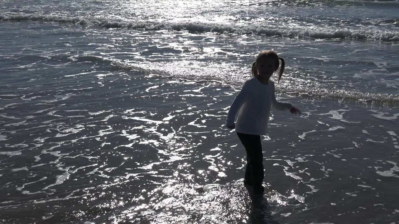 Child turning in the surf with sunlit foam around their feet.