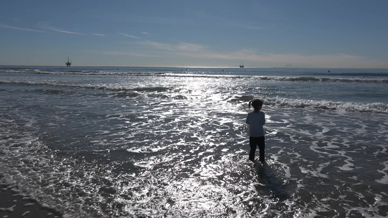 Girl standing in shallow water as foam spreads across the wet beach.