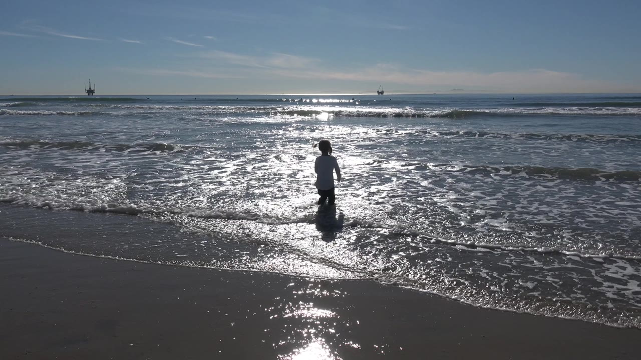 The child appears farther right in the frame, standing in foamy Huntington Beach water as small waves move toward the wet sand.