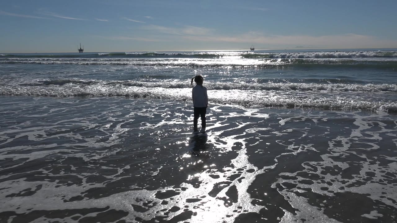 At two seconds, the child appears slightly silhouetted against strong sun reflection on the water, with waves breaking across the Huntington Beach horizon.