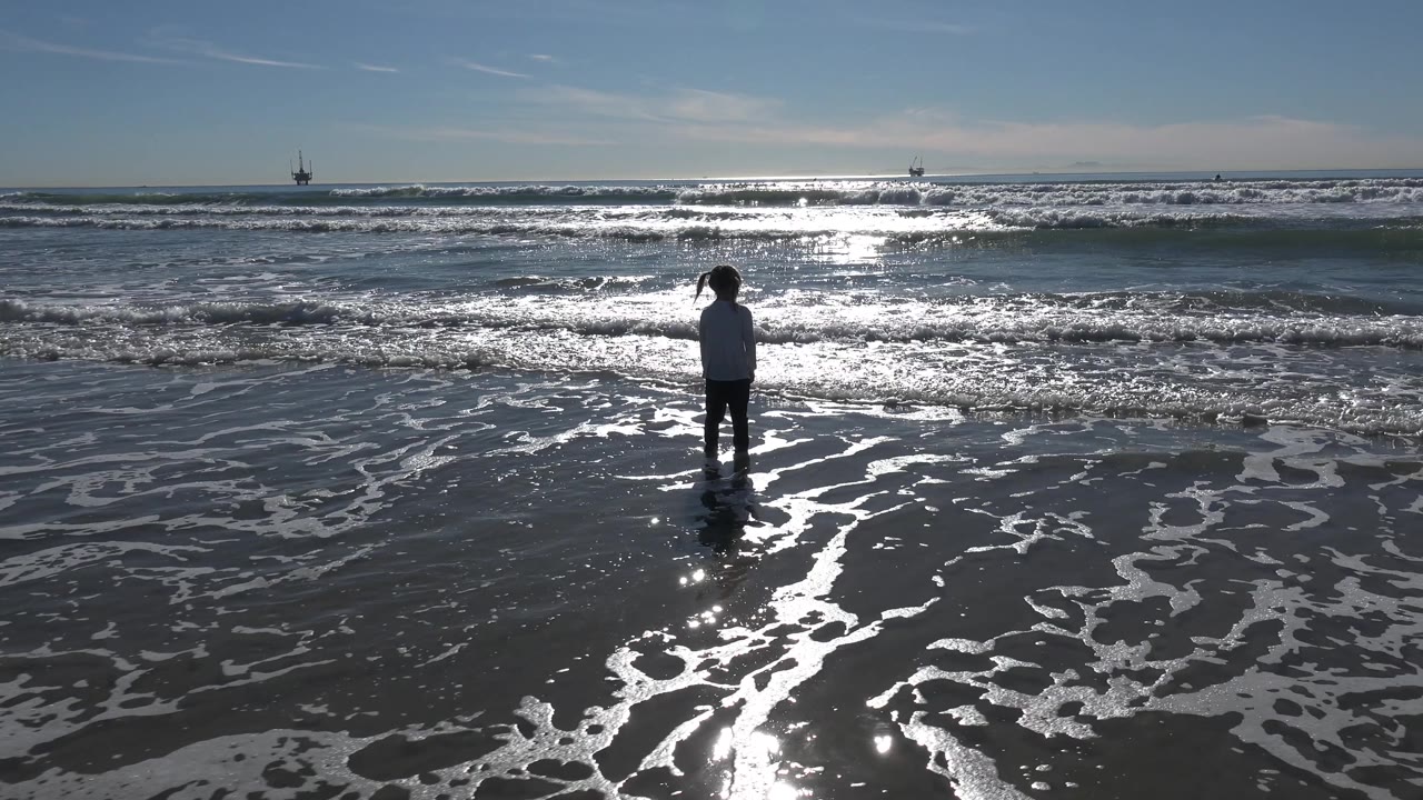 Child standing near foamy waterline with waves behind