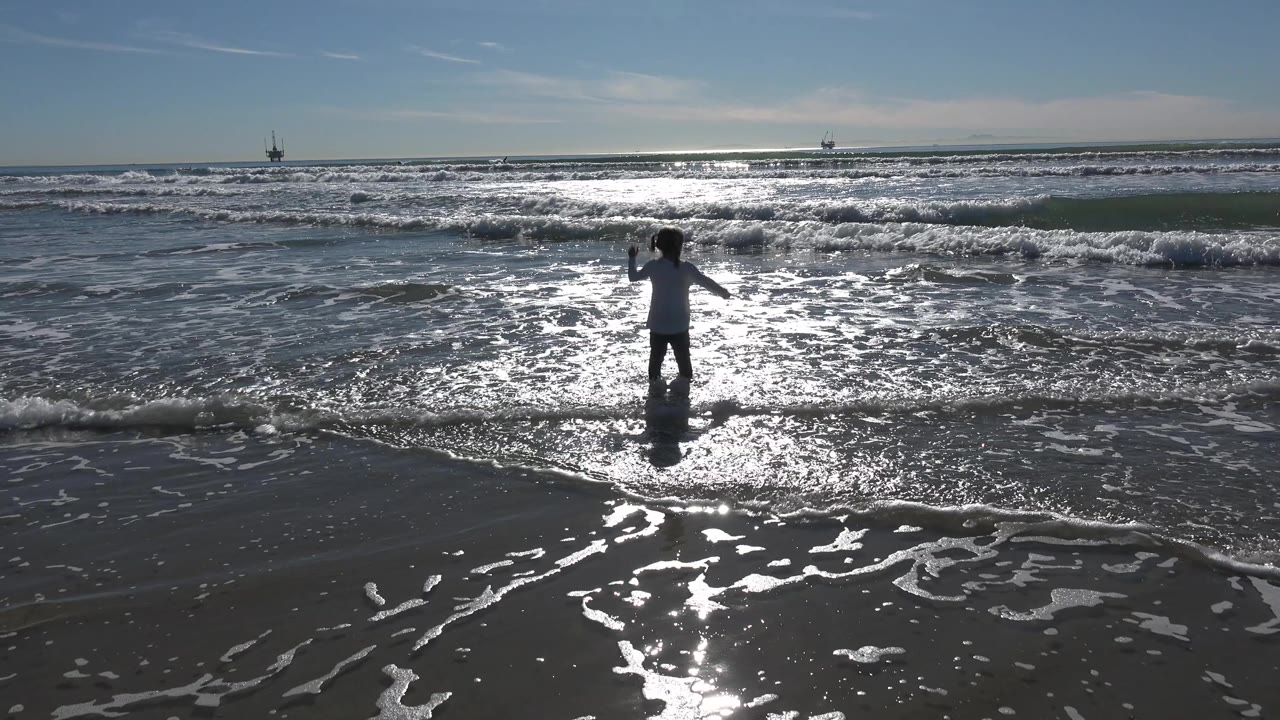 Young girl facing the ocean as waves break under strong backlight.