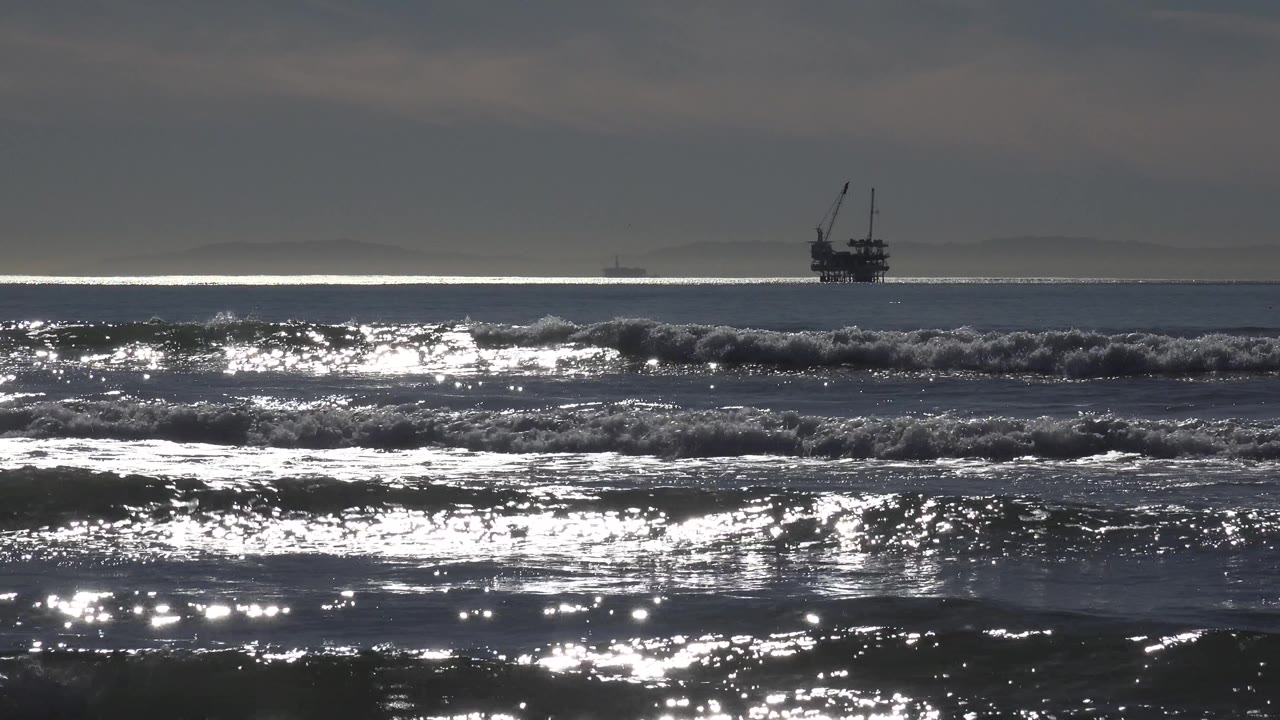 Dark surf with bright sun reflections and a distant offshore silhouette on the horizon.