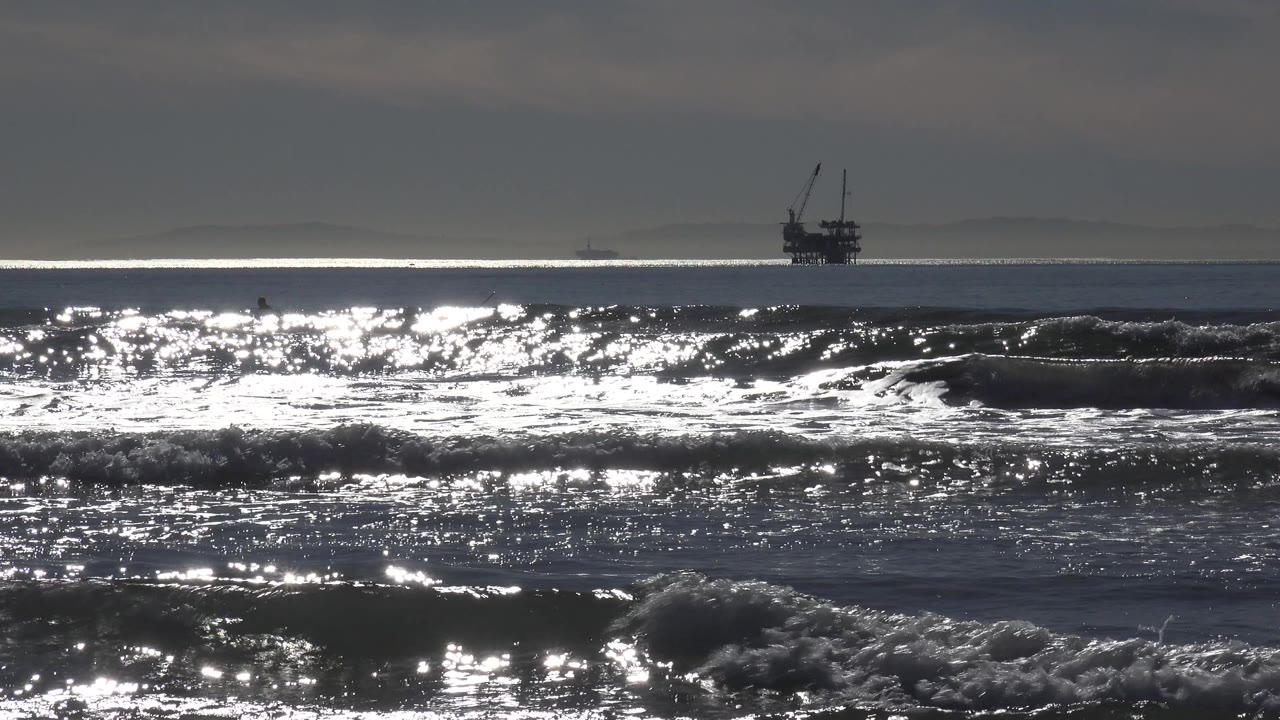 Distant ship silhouette beyond bright surf and rolling ocean waves.