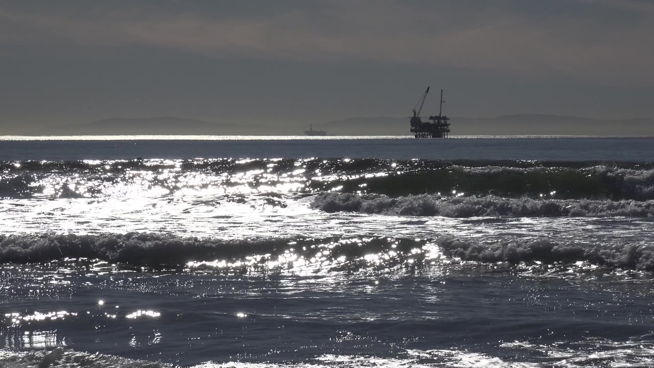 At Huntington Beach, the distant ship returns toward the left horizon while broad reflective surf bands fill the lower frame, with no visible people.