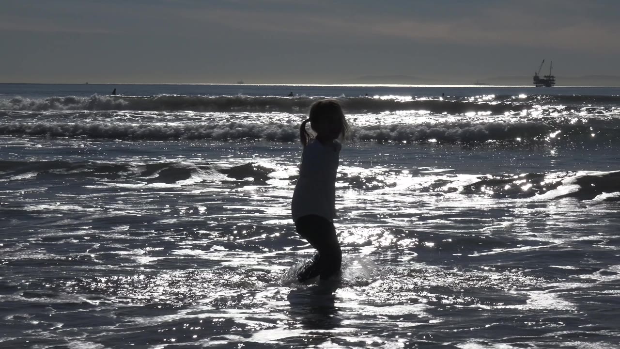 Young girl walking through shallow surf in side profile.