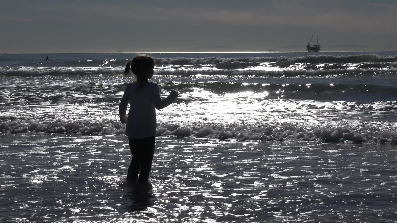 Child centered in wet sand with waves glittering behind her.