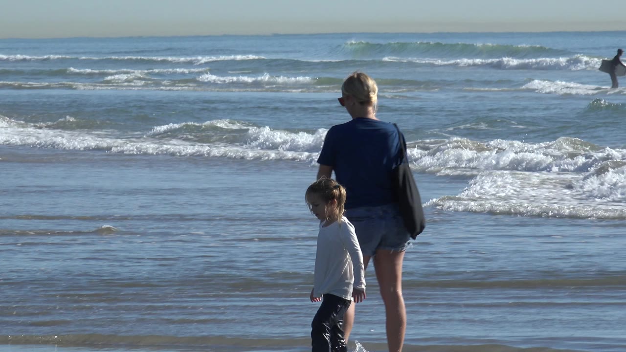 Woman and child face the surf on wet sand