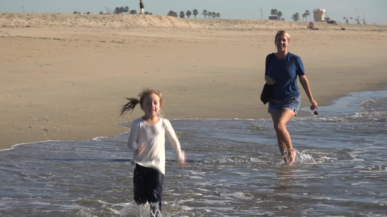 Young girl close to camera with adult woman behind in shallow surf.