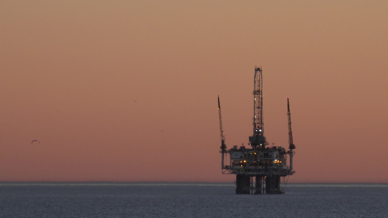 A distant offshore platform remains centered over the water near Huntington Beach, with a darker ocean band and no visible people.