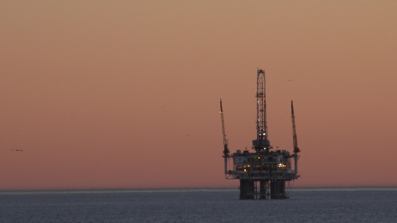Oil platform shape against pink-orange sky over the ocean