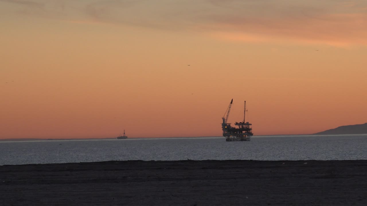 Calm ocean horizon with silhouetted offshore structure and dark beach foreground.