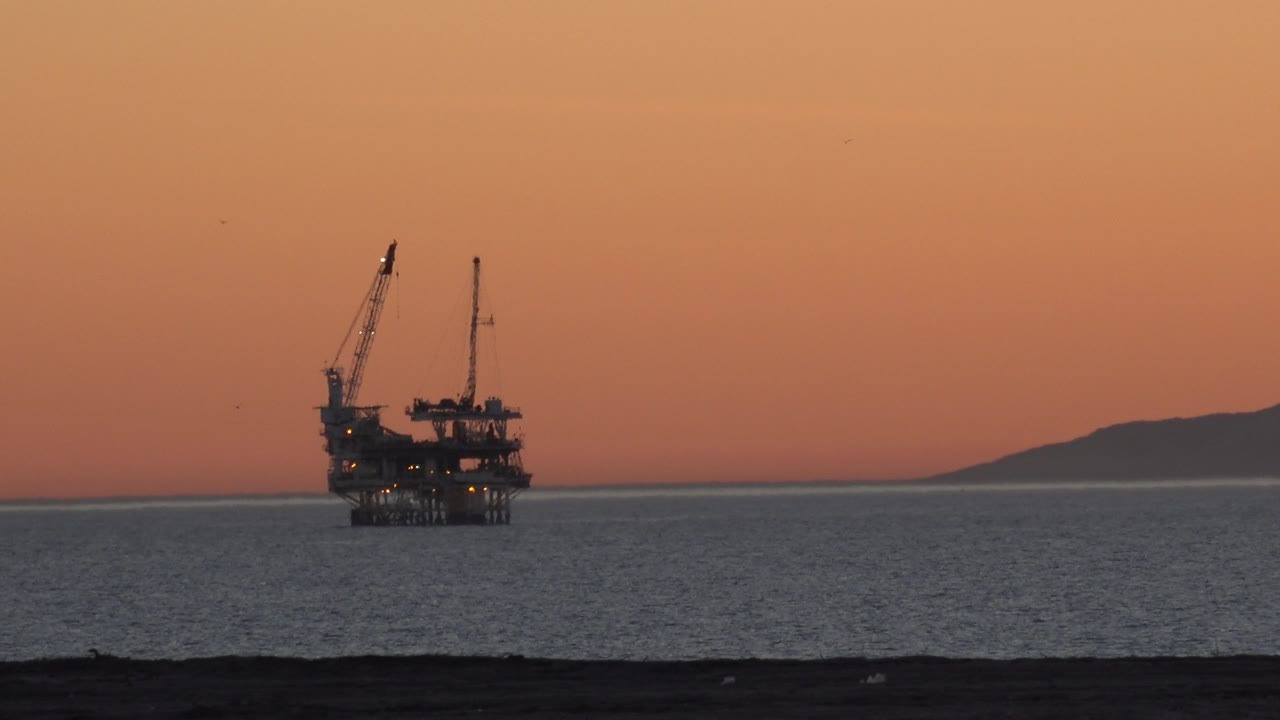 Industrial offshore structure silhouetted near the horizon at sunset.