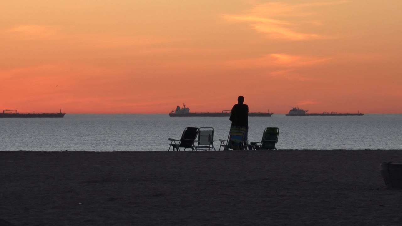 Two people and beach chairs silhouetted against sunset ocean