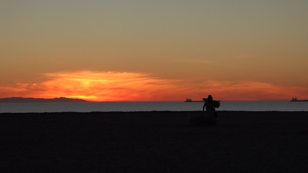 Sunset over a dark beach with a silhouetted person near the shoreline.