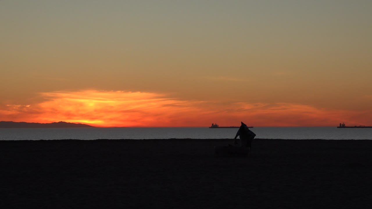 Silhouetted beach cleaner beside the ocean at sunset.