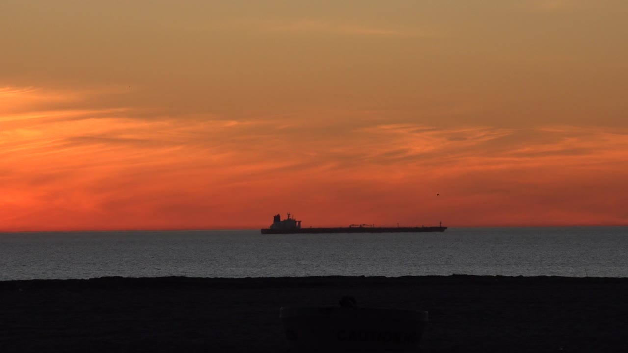 Orange sunset over the ocean with a cargo ship silhouette near the horizon.