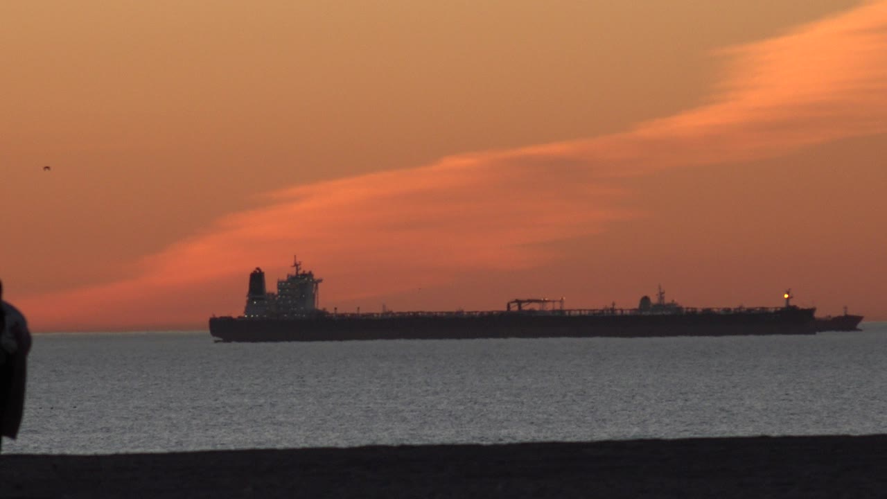 Cargo ship offshore under orange sunset clouds.