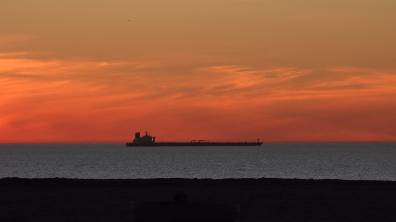 Long cargo ship silhouette under red-orange sunset sky