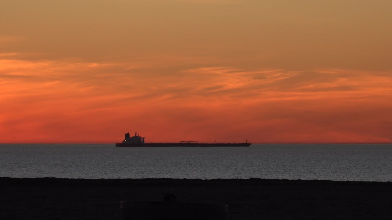 Tanker on the horizon with red-orange sunset light.