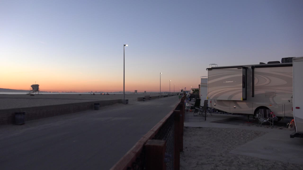 Beachside paved path at sunrise with RVs and light poles.
