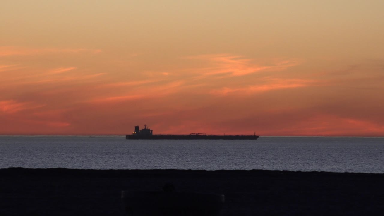 Cargo ship crossing a sunset horizon above dark beach foreground.