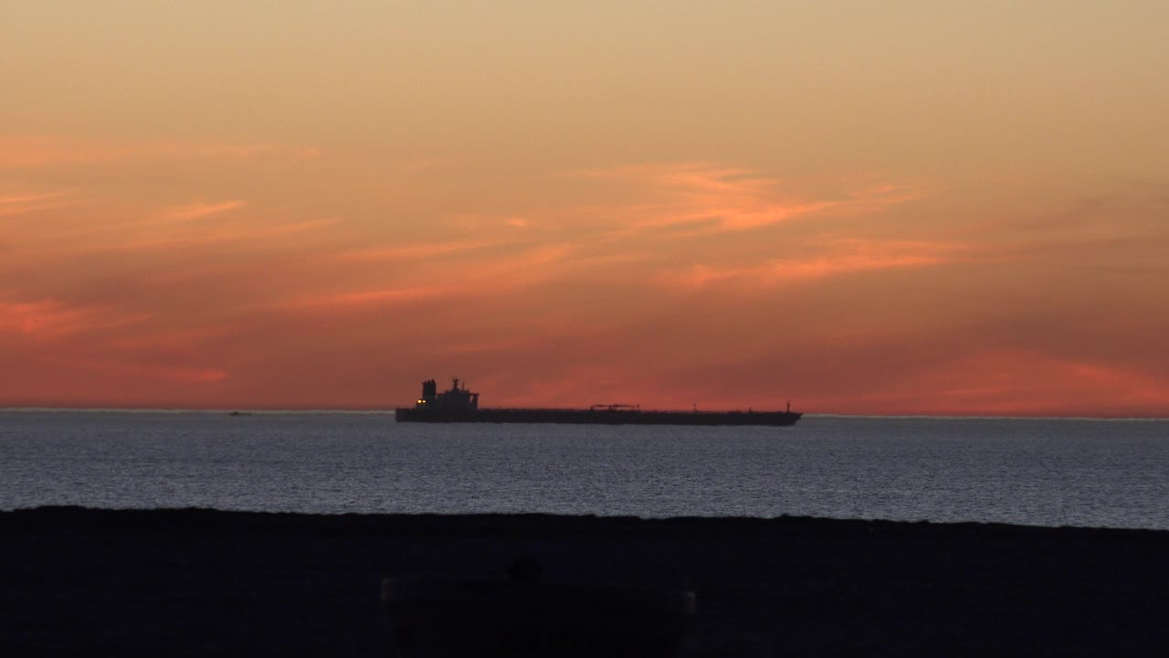 Tanker ship on the ocean under an orange sunset sky.
