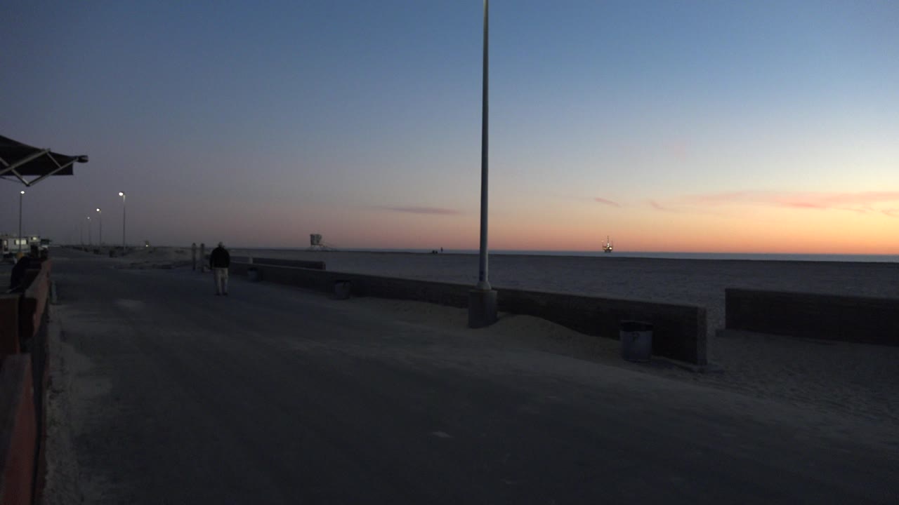 Dusk shoreline with a lone person walking away near the beach edge.