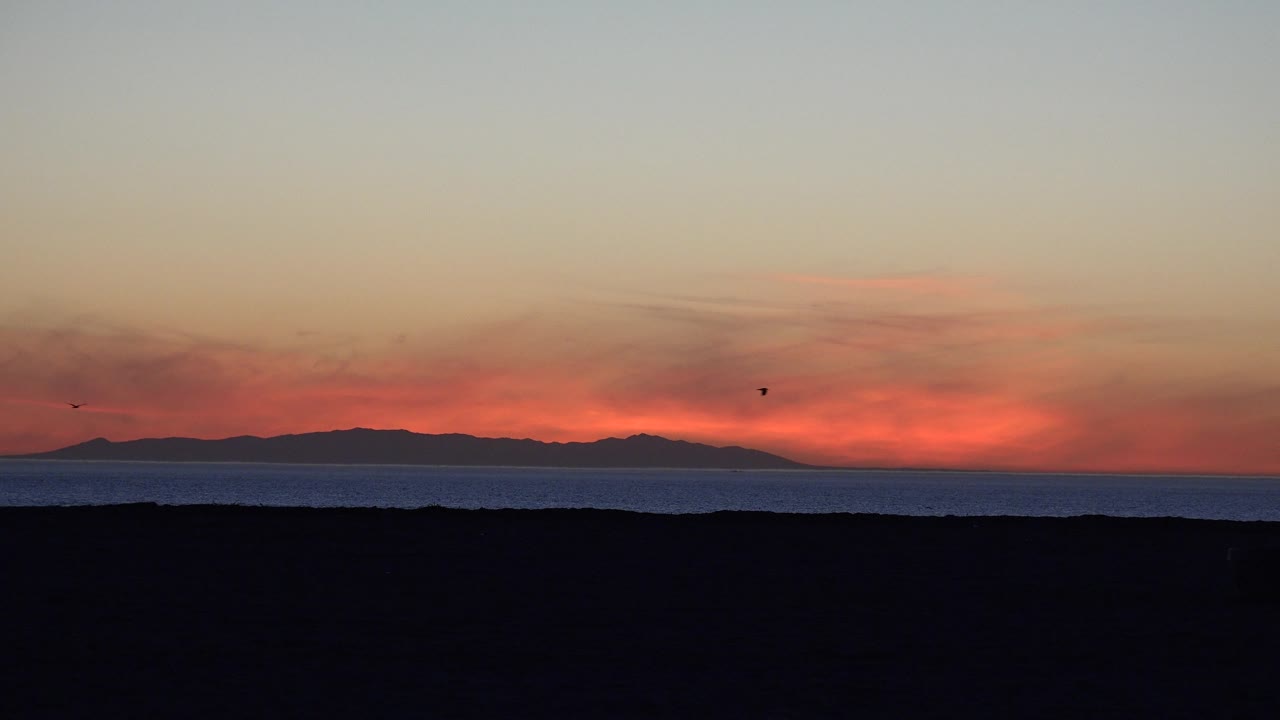 Dusk ocean scene with silhouetted land and a wide pale sky above.