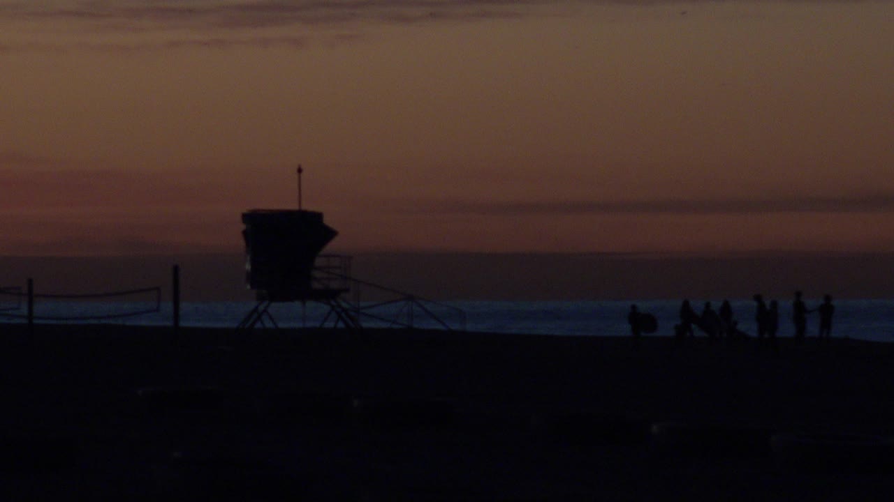 Beach tower silhouette with people spread along the shoreline.