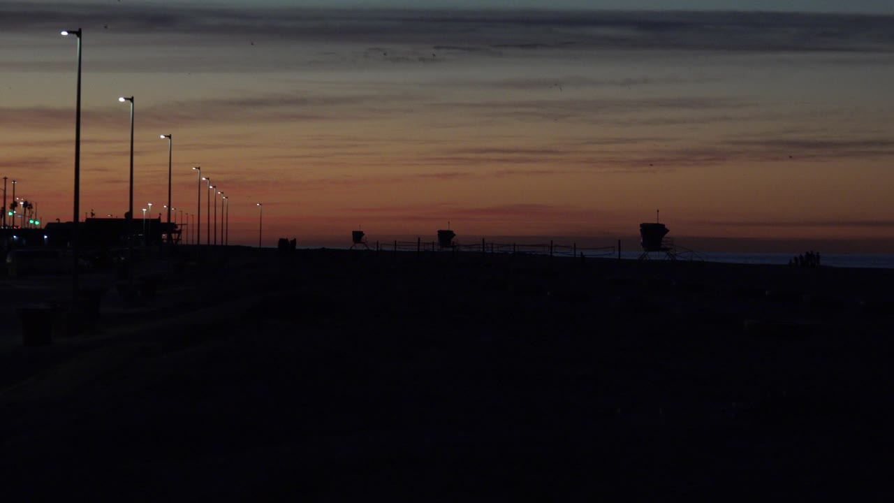 Empty dark waterfront scene with streetlights and layered sunset sky.