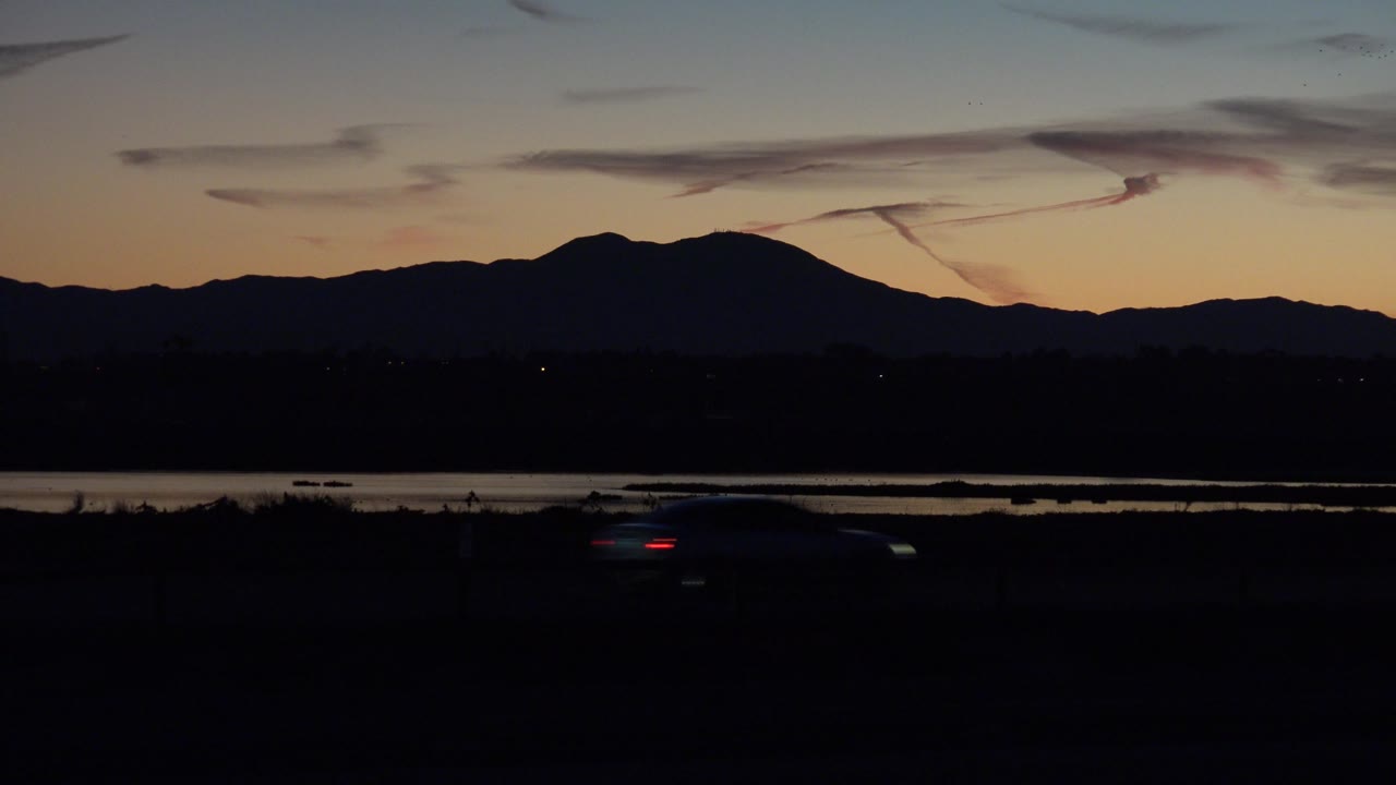 A car crosses the dark highway beneath silhouetted mountains at twilight.