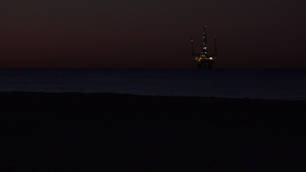 Huntington Beach shoreline view at twilight with the offshore structure more centered against the dark ocean and reddish sky, with no visible people.