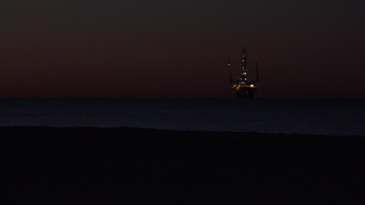 Distant offshore structure with lights at the right side of a dark ocean horizon.