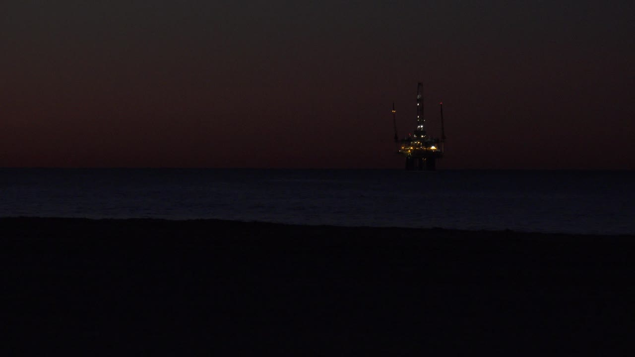Lit offshore structure near the right side above dark ocean water.