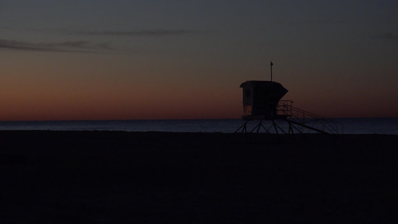 Lifeguard tower silhouette on a dark beach at sunset.