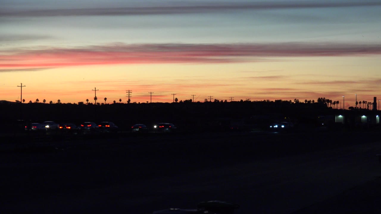 Dark highway traffic under an orange sunset sky.