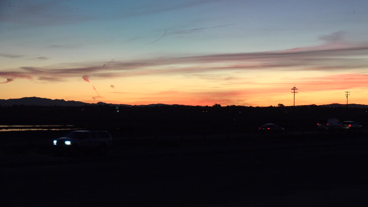 Vehicles move through a shadowed road scene at sunrise.