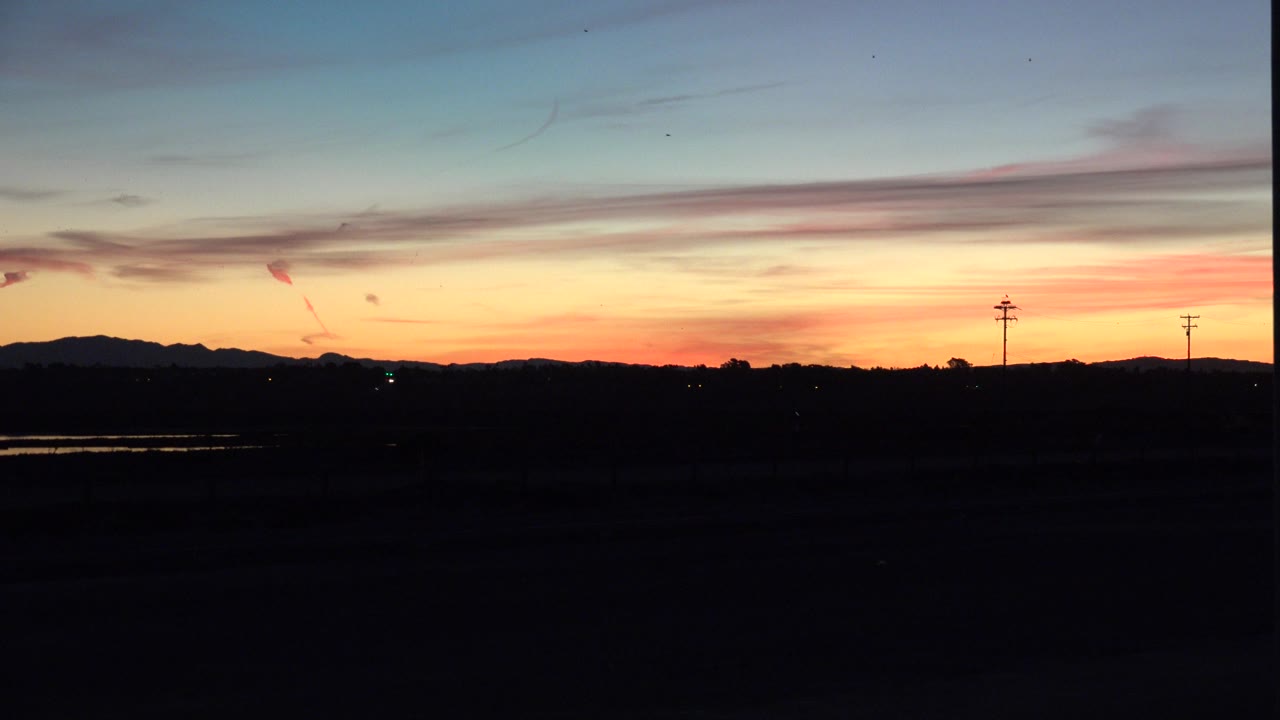 Opening frame of a Huntington Beach, California sunset with a blue upper sky, gold horizon glow, silhouetted land, distant utility poles, and no visible people.