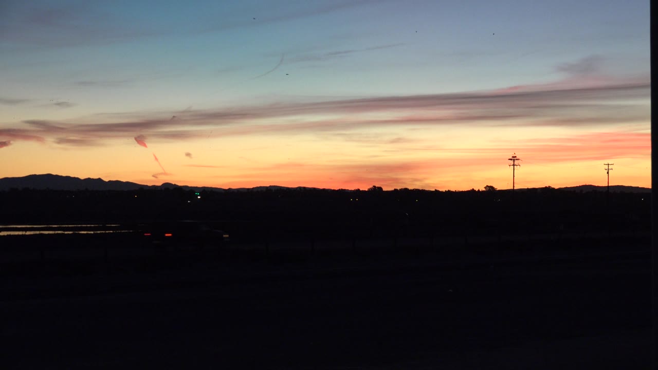 Sunset sky over dark land with small distant lights near the horizon.