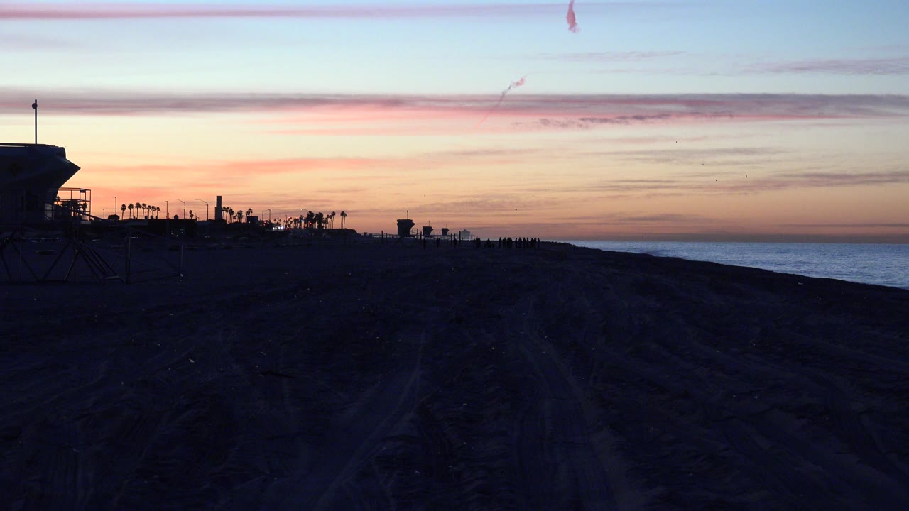 Dark beach tire tracks under a pastel sunset sky beside the ocean.
