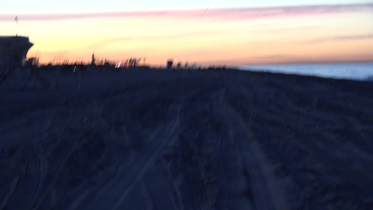 Dark beach at sunset with a silhouetted lifeguard tower and ocean horizon.