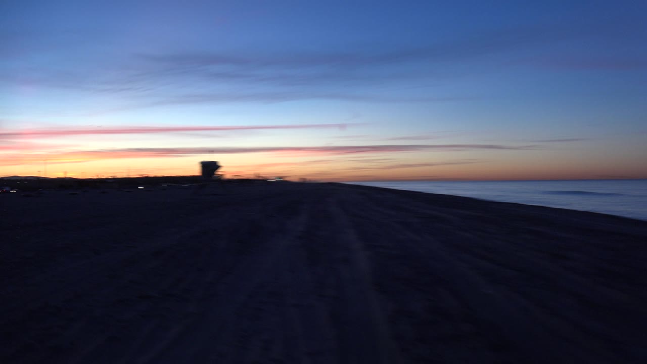 Wide dark shoreline with sunset colors and ocean at the right edge