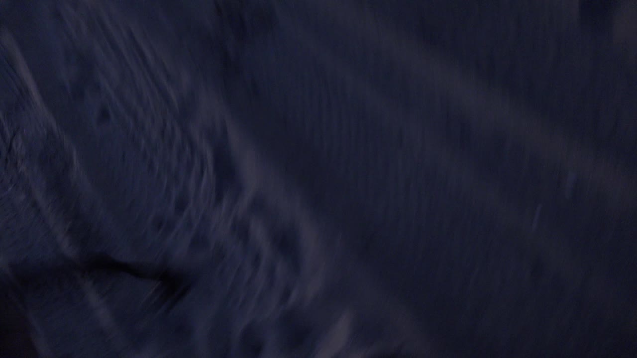 Dark close view of sand or fabric texture with a black object crossing the frame.
