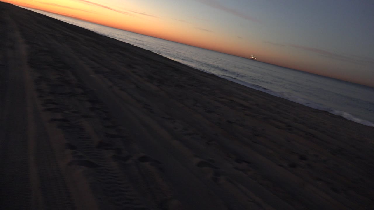 Beach tracks run toward a slanted sunset horizon beside the ocean.