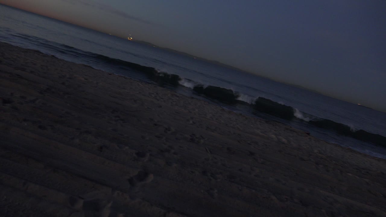 Huntington Beach surf forms narrow foam lines along the slanted shoreline, with dark footprint-marked sand below and no visible people.
